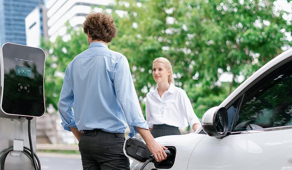 A man charging an electric car while a woman watches.