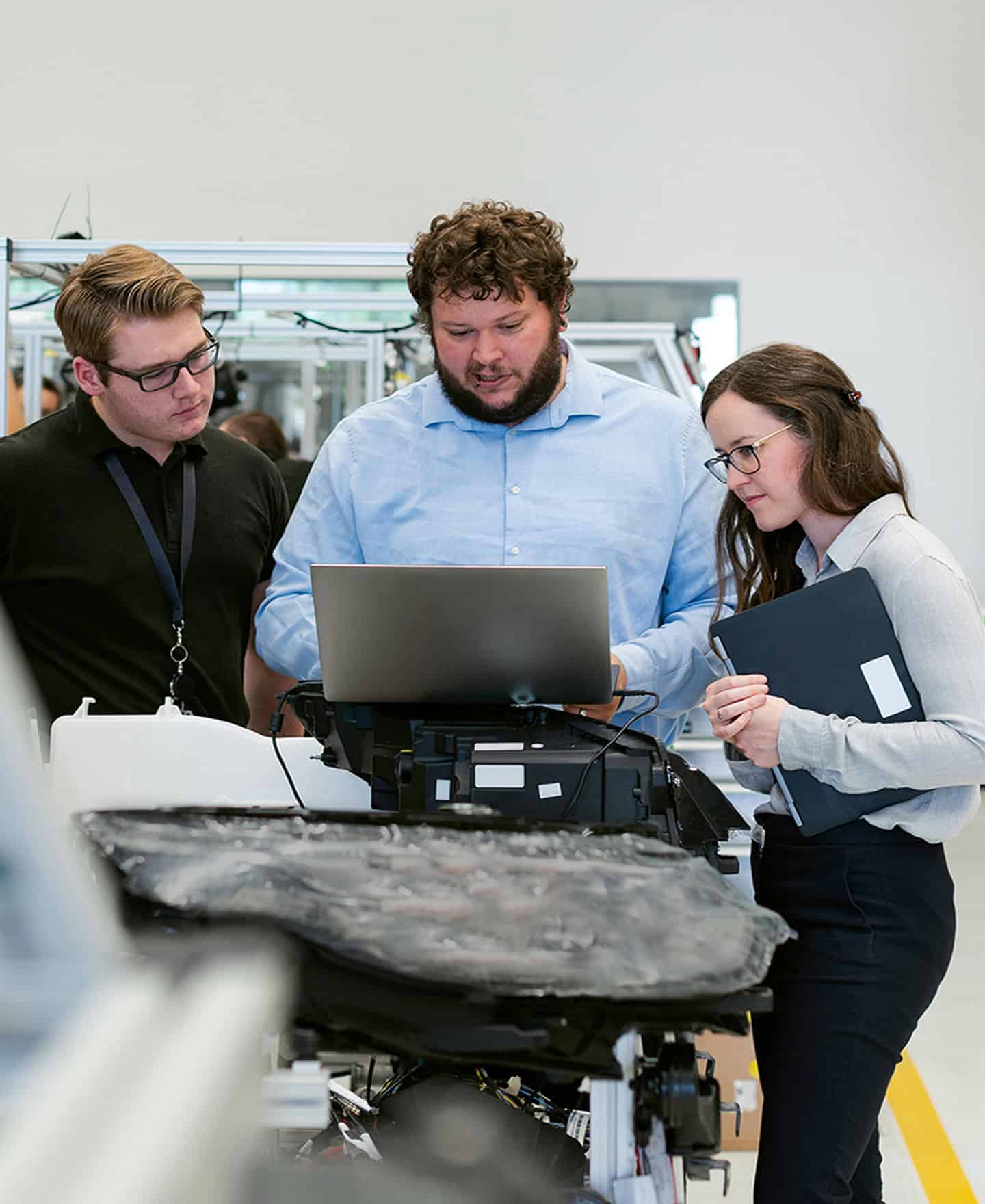 Three people staring at a laptop in a factory.