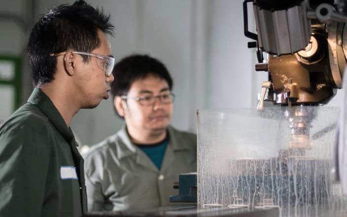 Two men watching an assembly robot on a factory floor.