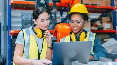 Two women wearing hard hats, with ear protectors and reflective vests.
