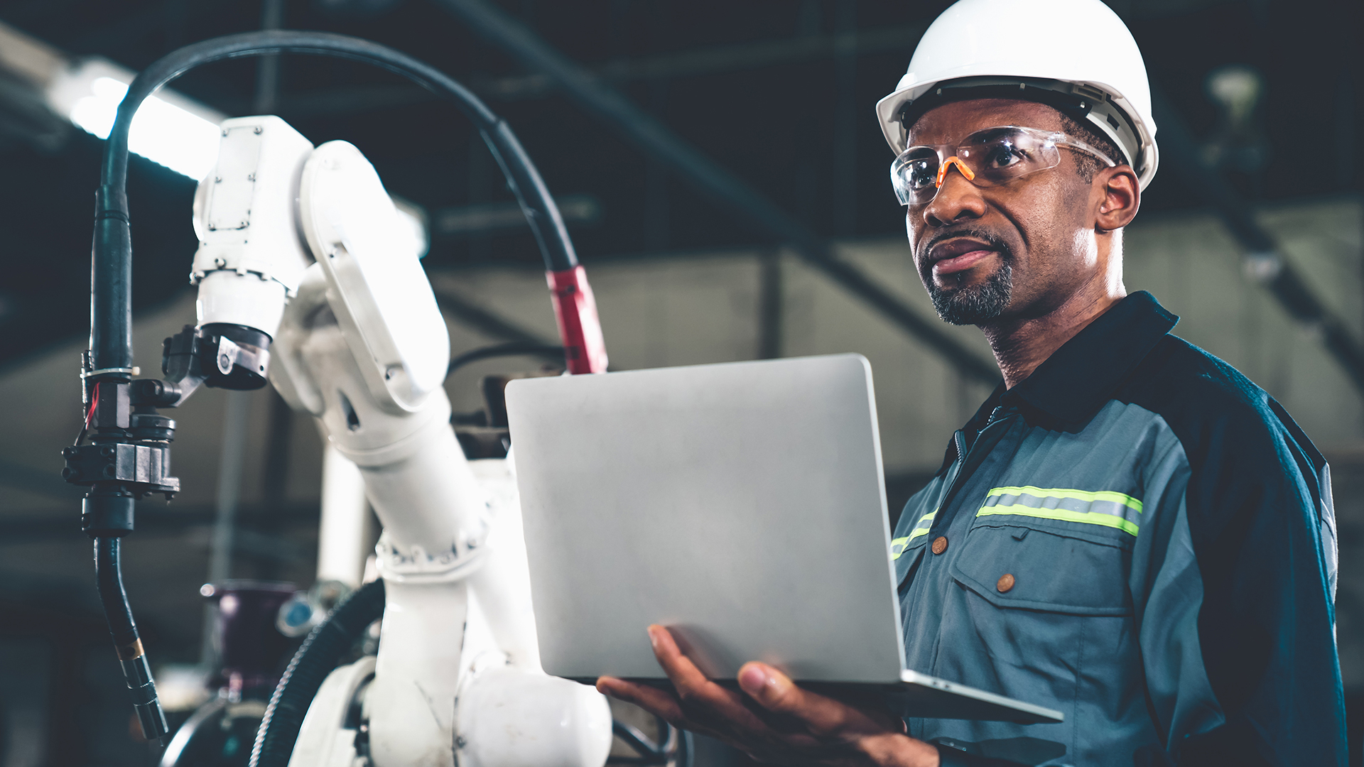 Man in a hard hat holding a laptop in a factory.