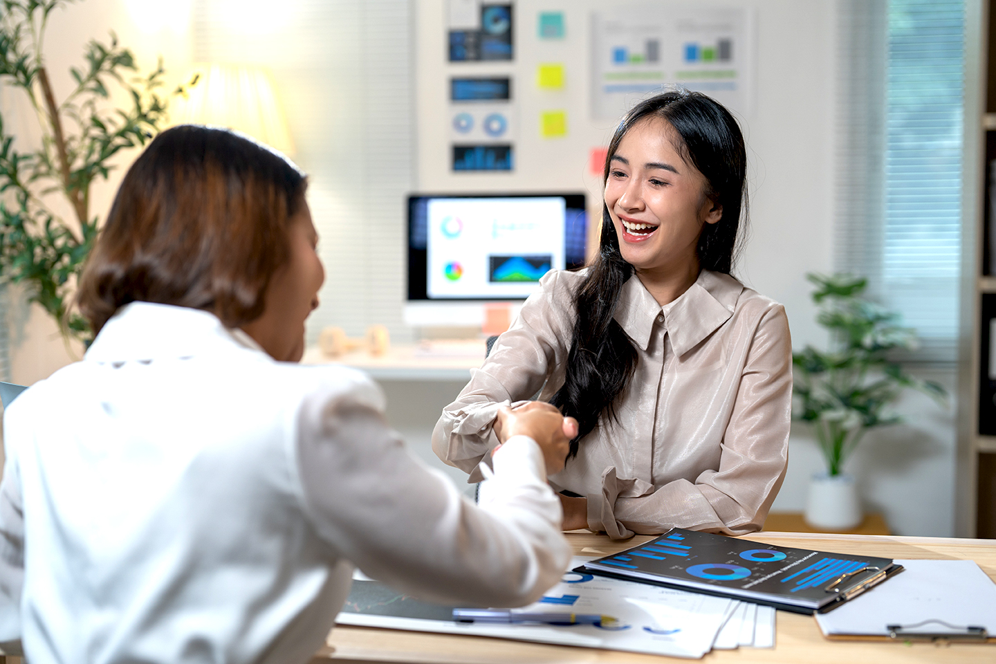 A woman in an office setting shaking hands and smiling at someone.