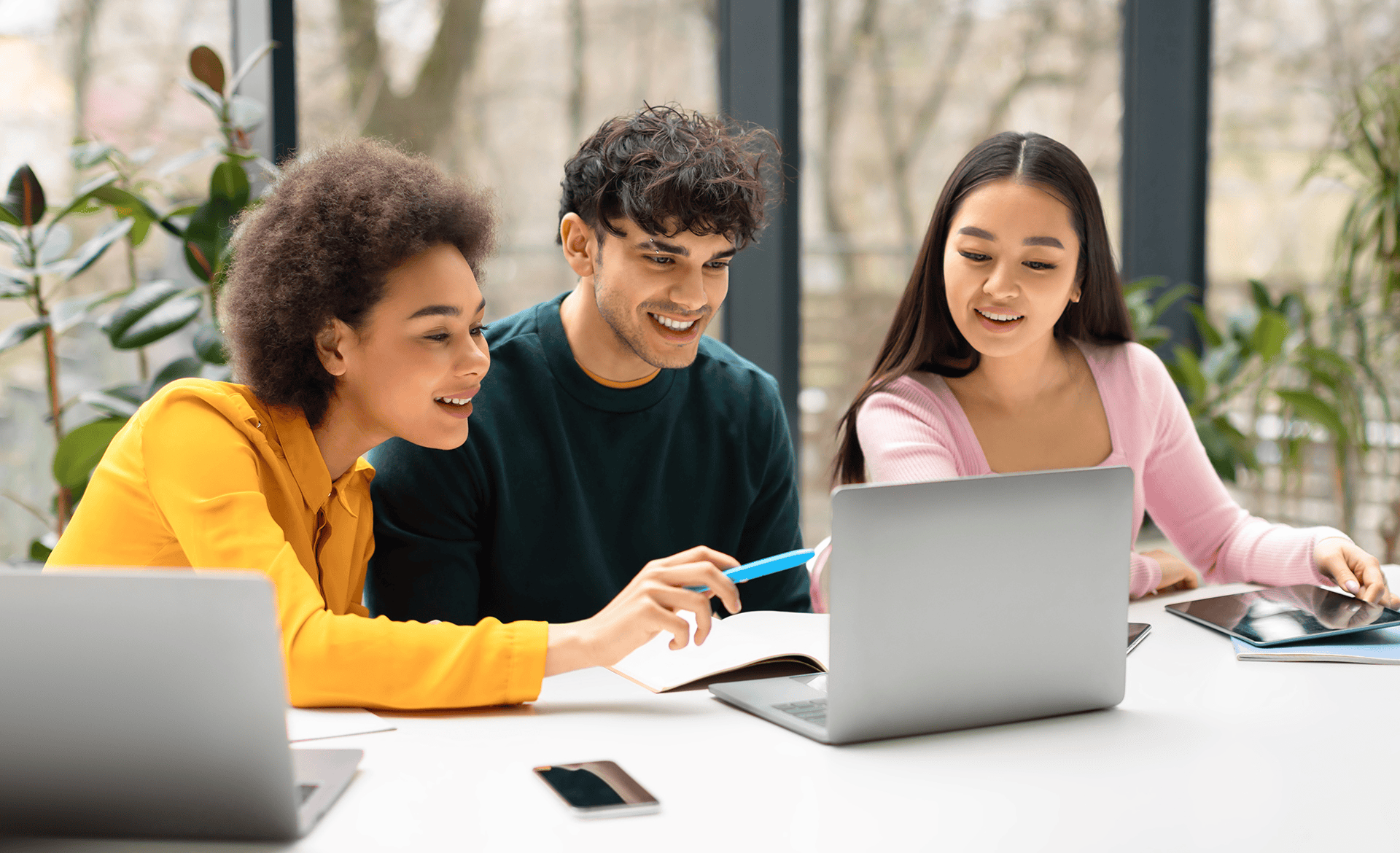 A man and two women sitting at a desk looking at a laptop.